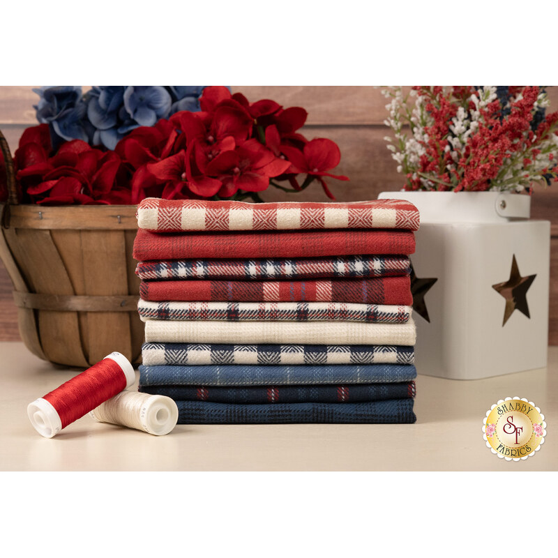 A stack of the flannel fabrics included in the Primo Plaids Americana FQ set, with flowers and a basket and thread.