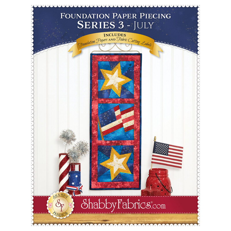 Front cover of the Foundation Paper Piecing Series 3 - July pattern showing the completed star and flag project in red, white, gold, and blue fabrics, staged on a golden craft hanger on a white paneled wall.