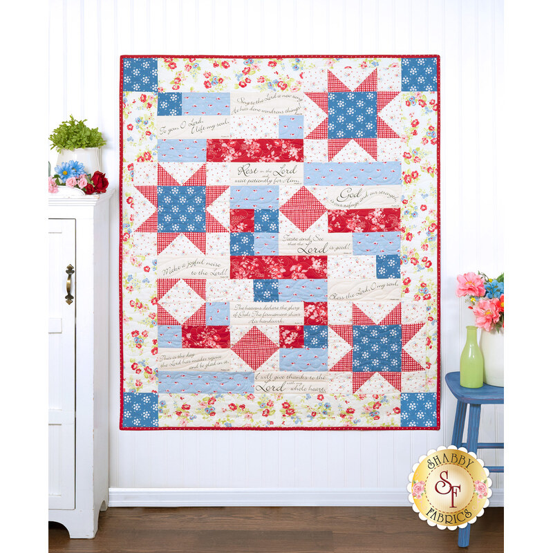 The Comfort of Psalms Quilt - Hollyhocks & Roses in red, blue, and cream, displayed against a light wall next to surrounding decor