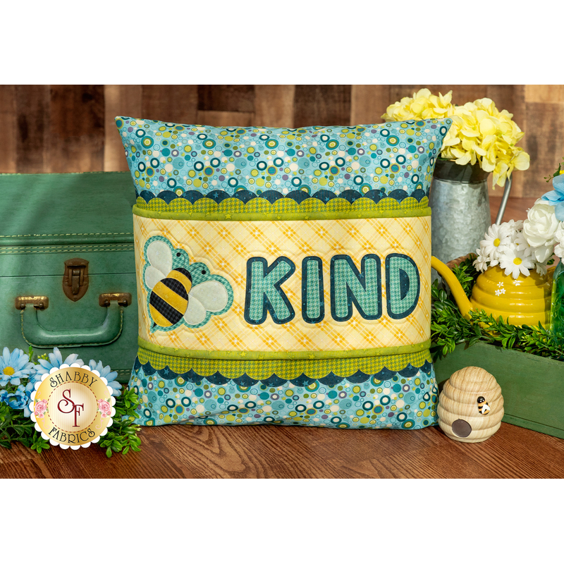 The finished June pillow wrap kit, a yellow wrap with blue and green scalloped borders and an appliqué bee beside appliqué letters that read 