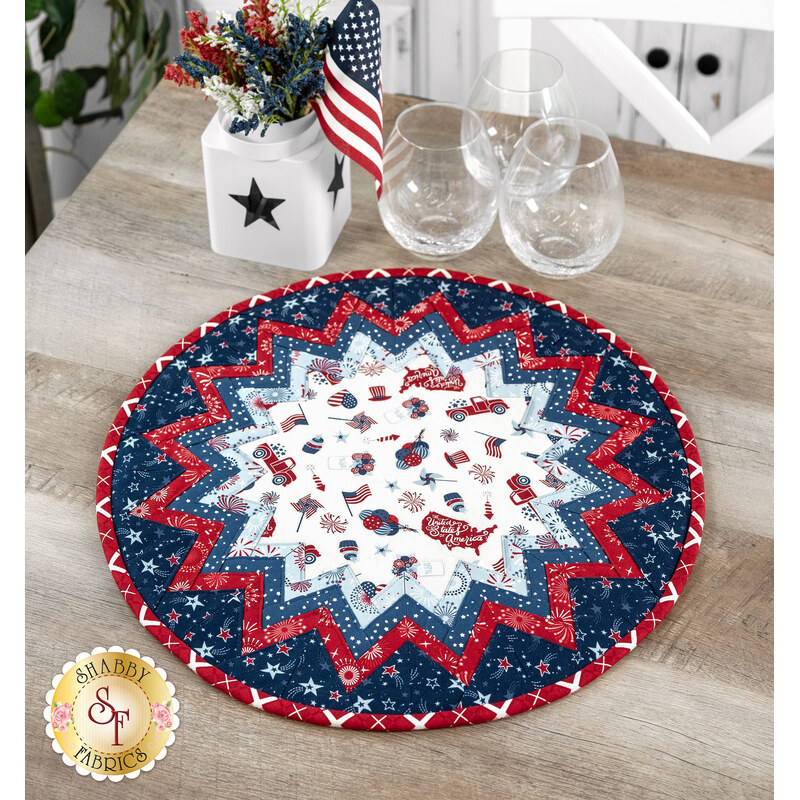 The Stars and Stripes Forever table topper with a star pattern, featuring red, white, and blue designs on a wooden table next to coordinating decor.