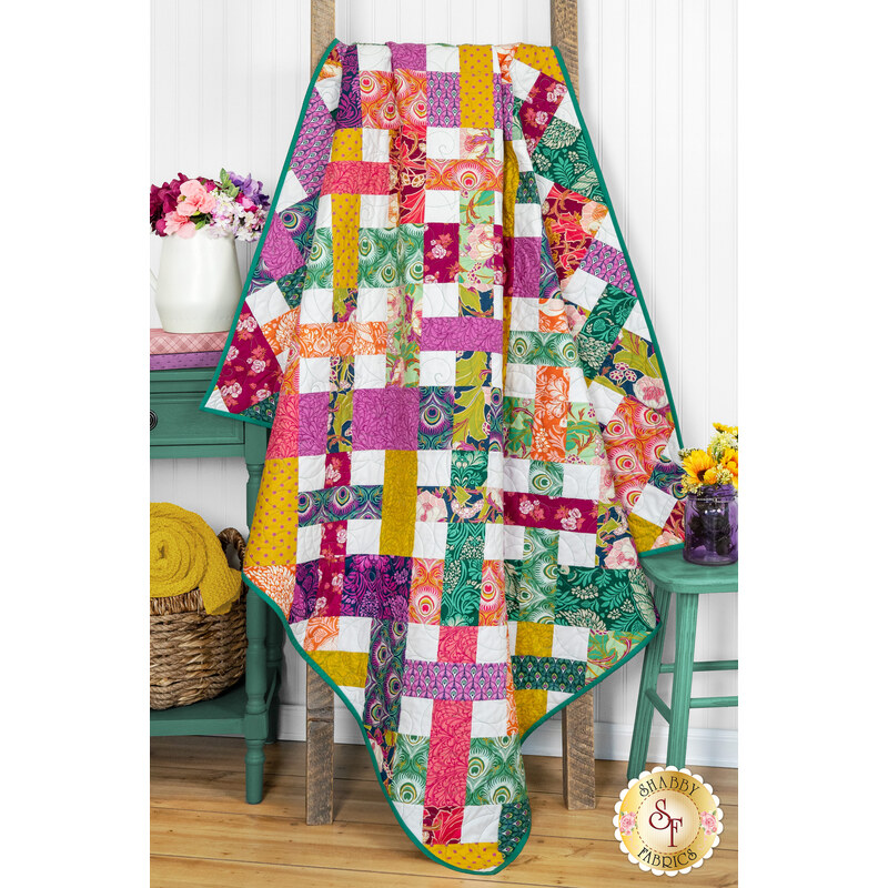 The completed Picnic Quilt colored in vibrant fabrics from the Wild Abandon collection, staged on a quilt ladder with coordinating furniture and flowers.