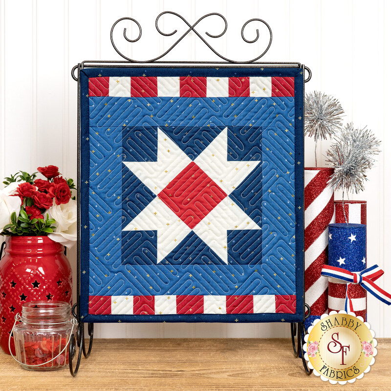 The completed Star Spangled project hung on a metal stand bordered by coordinating summer flowers and patriotic decor.