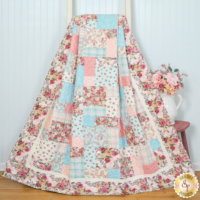 A colorful patchwork quilt featuring floral and pastel patterns, draped over a wooden ladder.