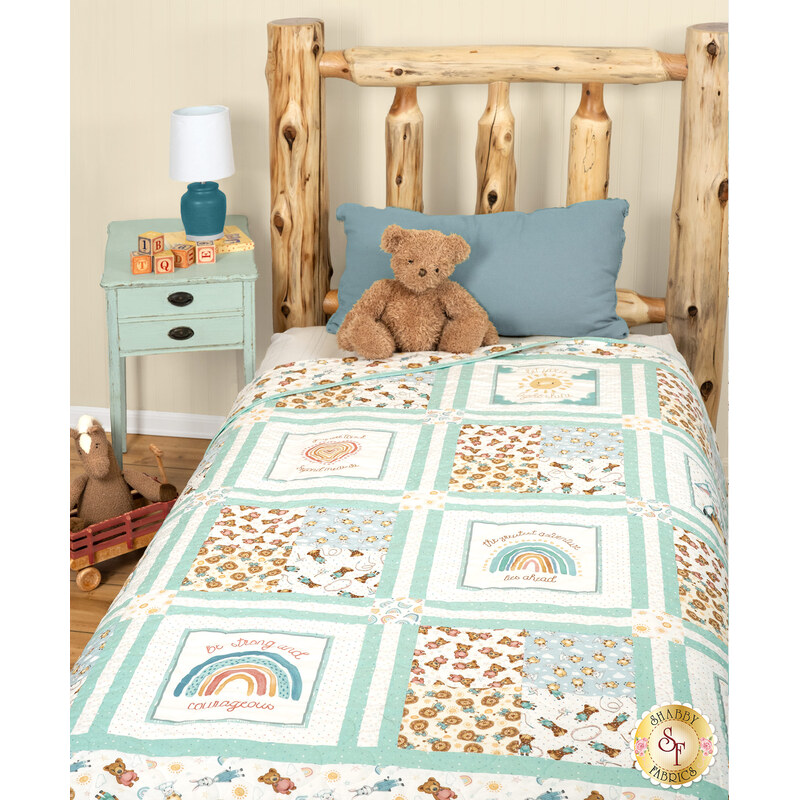 A shot of the quilt draped over a cabin bed, staged with a teddy bear and ABC blocks on a coordinating aqua nightstand.