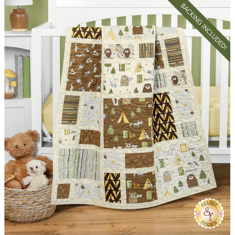 A patchwork quilt in the neutral brown and tan tones from the Into the Woodlands collection draped over a white crib, set with coordinating baby toys and decor. 