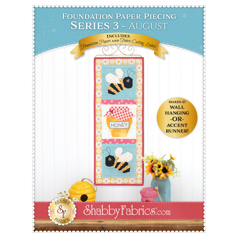 Front cover of the Foundation Paper Piecing Series 3 - August pattern showing the completed bee and honeypot project in yellow, red, and blue fabrics, staged on a golden craft hanger on a white paneled wall.