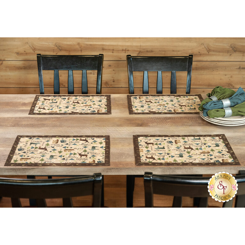A wide shot of the four placemats on a wooden table with coordinating cloth napkins off to the side on a stack of plates.
