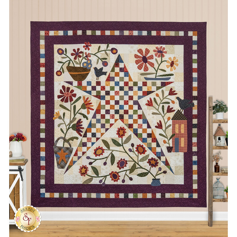 The completed Stellar Garden Quilt, colored in rich fabrics from the Flossie's Flowers collection by Henry Glass Fabrics. The quilt is hung on a warm beige paneled wall and staged with coordinating farmhouse decor.