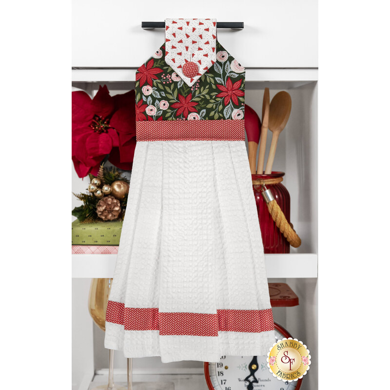 The completed hanging towel, colored in green and red fabrics from the Berry & Pine collection by Moda Fabrics, hung on a kitchen drawer and staged with coordinating decor.