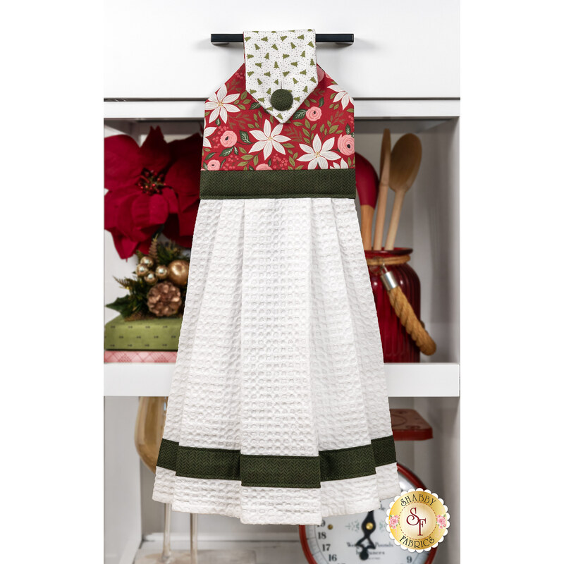 The completed hanging towel, colored in red and green fabrics from the Berry & Pine collection by Moda Fabrics, hung on a kitchen drawer and staged with coordinating decor.
