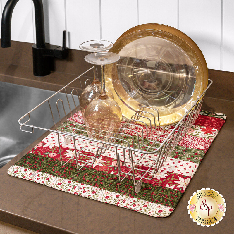 The completed Dry Ideas project, colored in red & green fabrics from the Berry & Pine collection, staged on a kitchen counter beside the sink and underneath a wire dish rack holding coordinating clean dish ware.