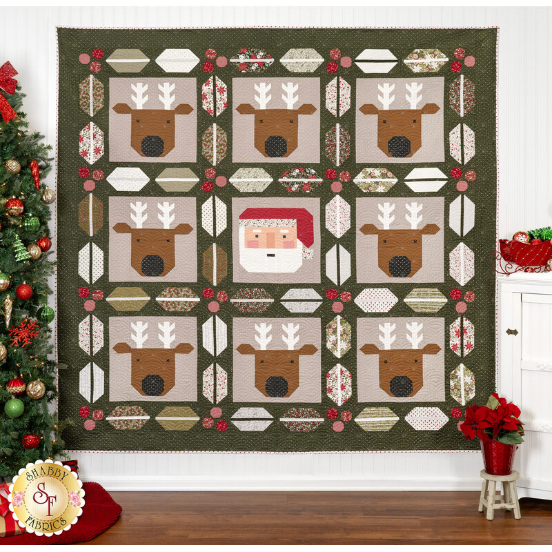 The Christmas Crew quilt featuring reindeer and Santa blocks, displayed near a Christmas tree and decorations.