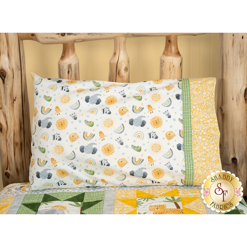 A shot of the Magic Pillowcase in white, yellow, and green, staged on a bed with a matching patchwork quilt in a cabin setting.