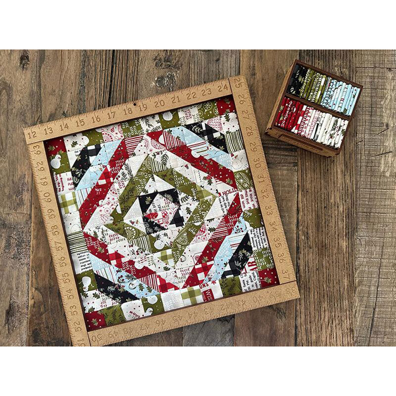 The completed mini quilt in a ruler frame using the Emmitt & Ivy collection Little Box fabrics, staged on a rustic wood surface.