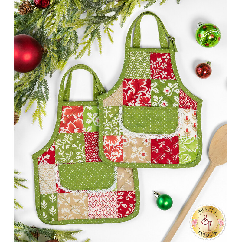 The two completed hot pads colored in bright green, red, and cream fabrics, from the Buon Natale collection, staged on a clean white background with coordinating holiday decor and a wooden spatula.
