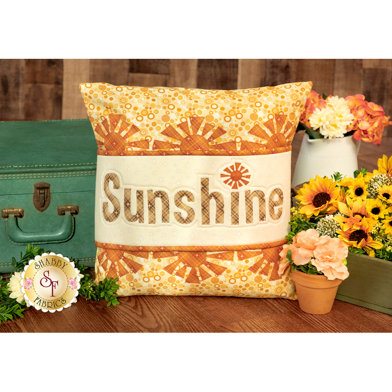 The finished August pillow wrap kit, a cream and orange wrap with orange sunshine borders and appliqué letters that read 