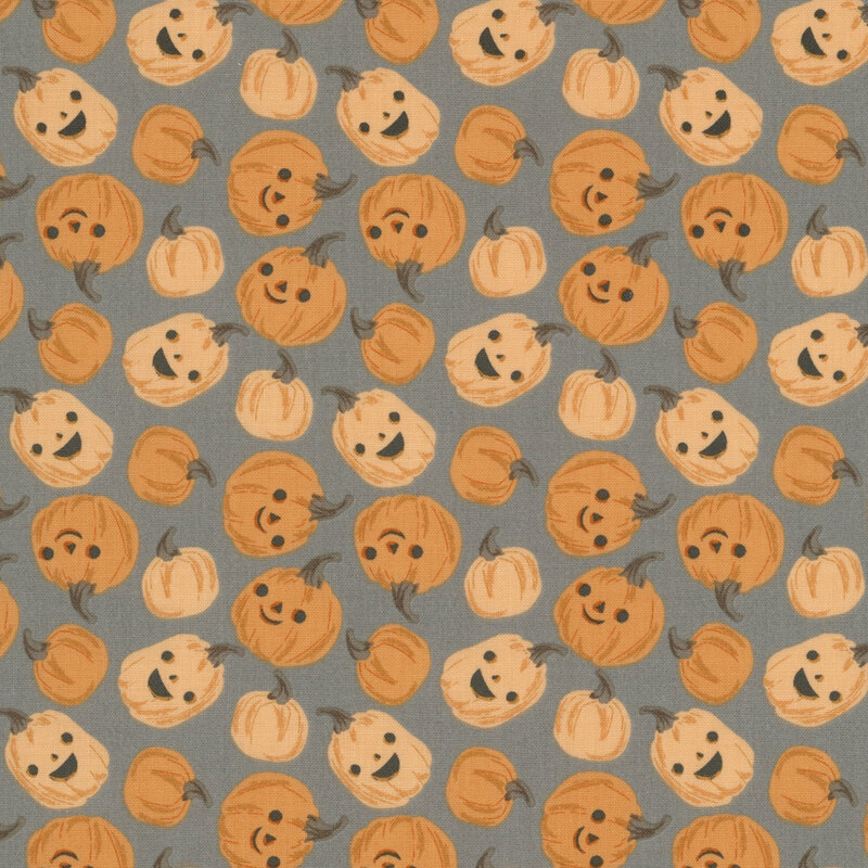 This dark gray fabric features scattered playful pumpkins with smiling jack-o’-lantern faces.