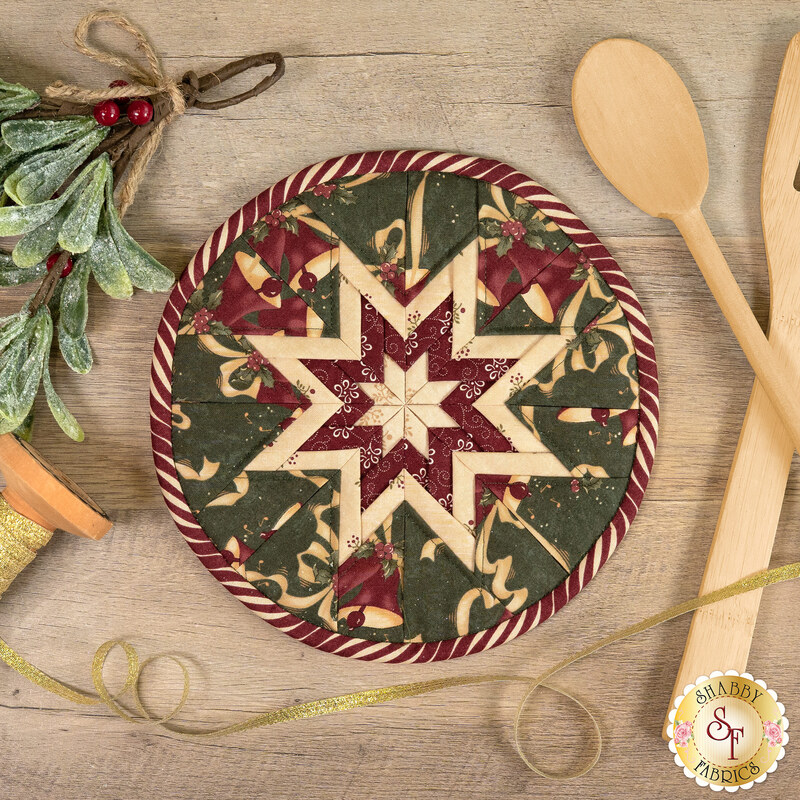The completed round green Folded Star Hot Pad, staged on a wooden table with coordinating seasonal and kitchen décor.