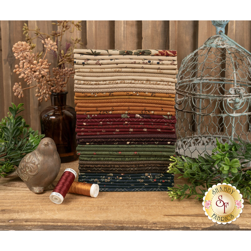 A stack of the fabrics featured in the Quail Run FQ set, with a bird and a birdcage and plants and thread.