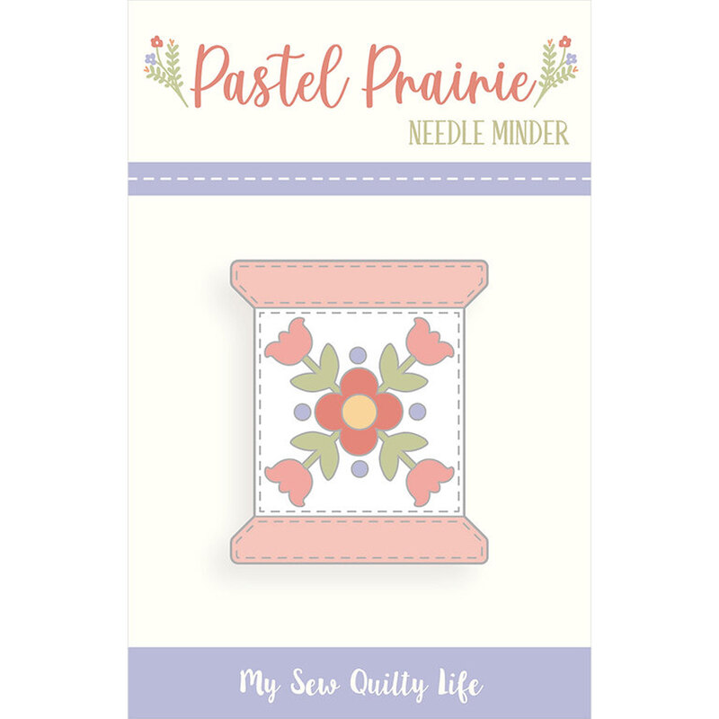 A digital image of a metal needle minder in the shape of a thread spool in its packaging with a floral design from the Pastel Prairie collection.