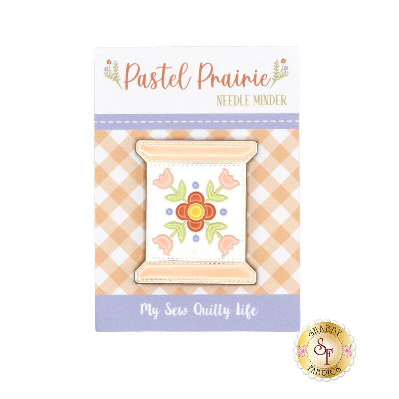 image of a metal needle minder in the shape of a thread spool in its packaging with a floral design from the Pastel Prairie collection.