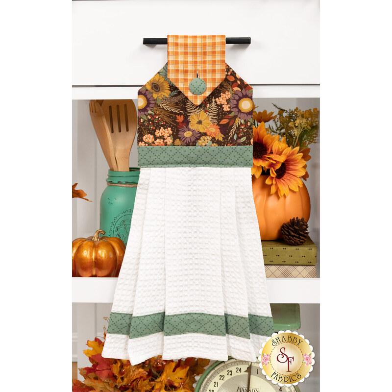 The completed Hanging Towel colored in brown, orange, and green fabrics from The Awe of Autumn collection, staged on a kitchen drawer with coordinating decor.