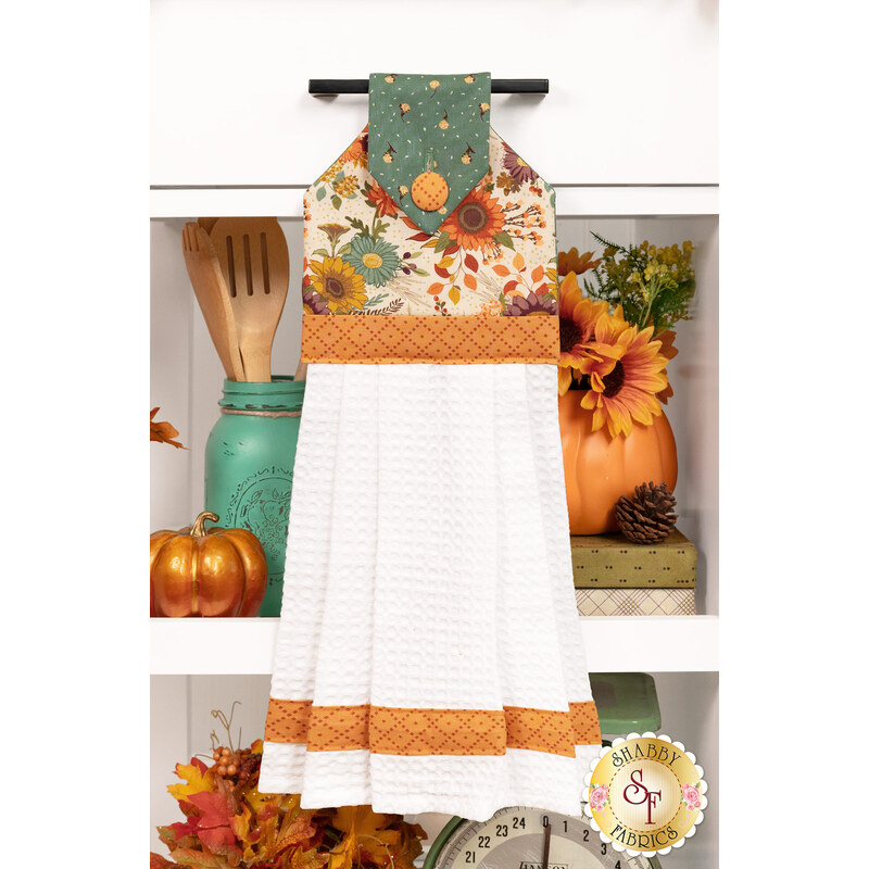 The completed Hanging Towel colored in cream, orange, and teal fabrics from The Awe of Autumn collection, staged on a kitchen drawer with coordinating decor.