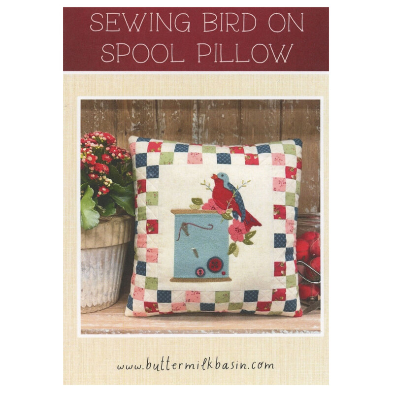 The front cover showing an showing the completed wall hanging pattern of a ball jar filled with sewing tools with a border of thread spools.