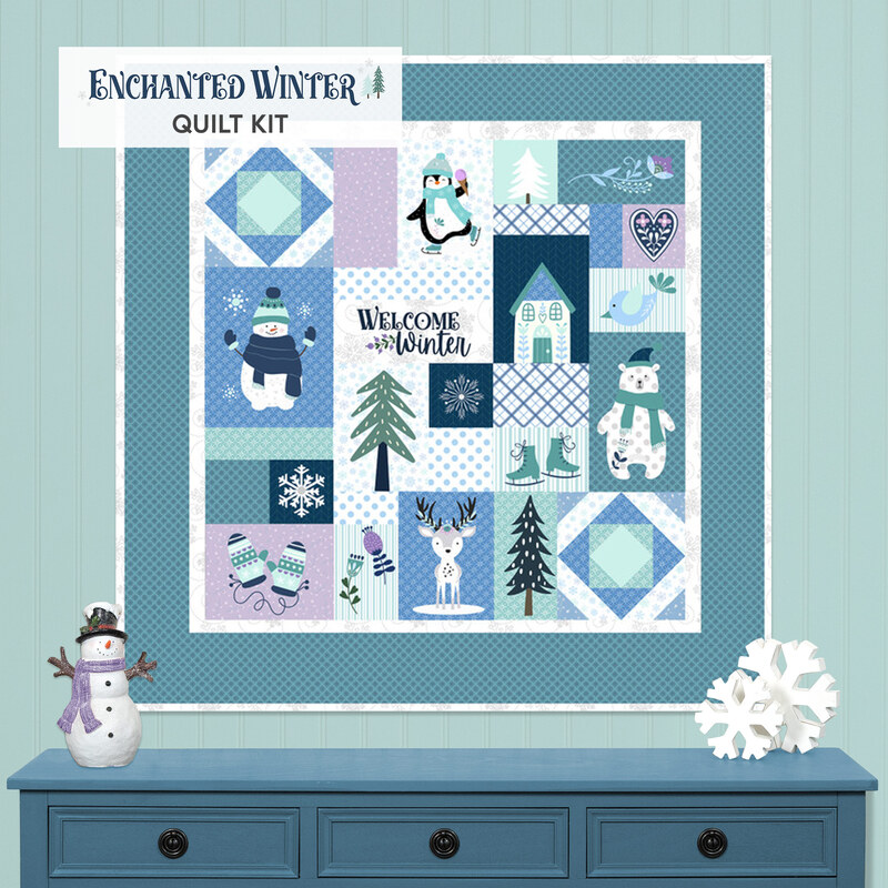 The Enchanted Winter Quilt, featuring blocks of winter woodland animals in teal, blue, white, and purple, hung on a teal paneled wall above a blue table staged with a snowman figurine and decorative snowflakes.