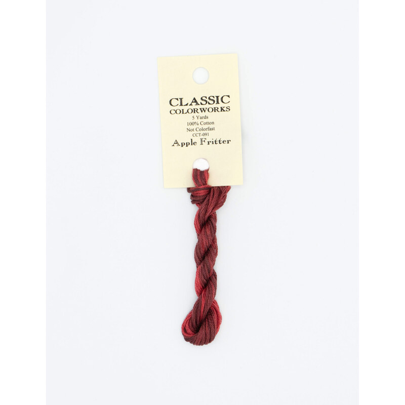 A skein of variegated red embroidery floss, twisted and bundled, with a cream and black label featuring the brand name and color information.