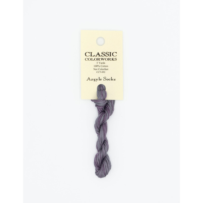 A skein of variegated purple and muted purple embroidery floss, twisted and bundled, with a cream and black label featuring the brand name and color information.