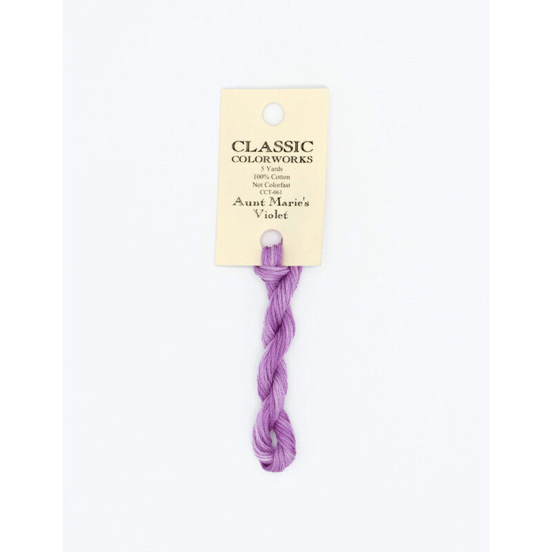 A skein of purple variegated embroidery floss, twisted and bundled, with a cream and black label featuring the brand name and color information.