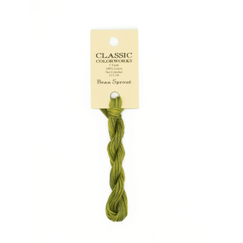 A skein of green embroidery floss, twisted and bundled, with a cream and black label featuring the brand name and color information.