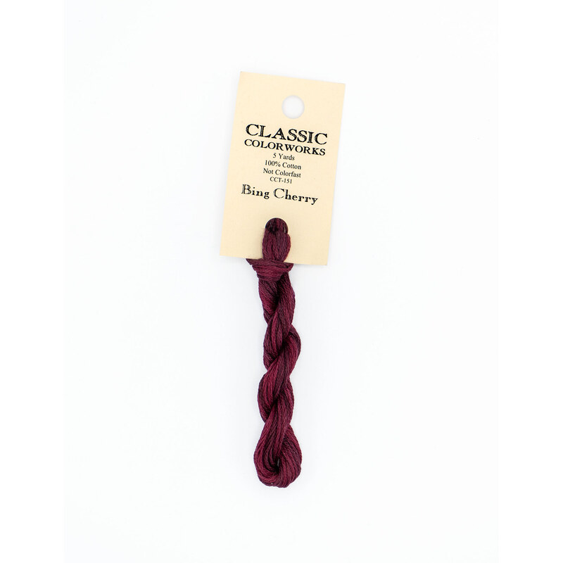 A skein of dark red embroidery floss, twisted and bundled, with a cream and black label featuring the brand name and color information.