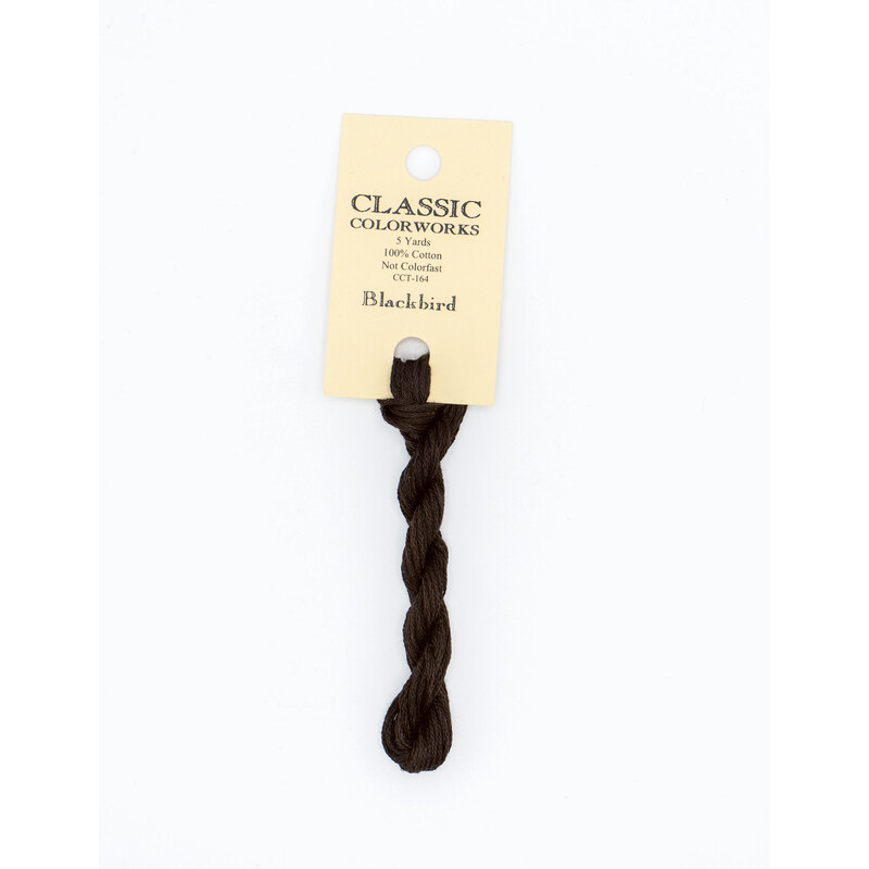 A skein of black embroidery floss, twisted and bundled, with a cream and black label featuring the brand name and color information.