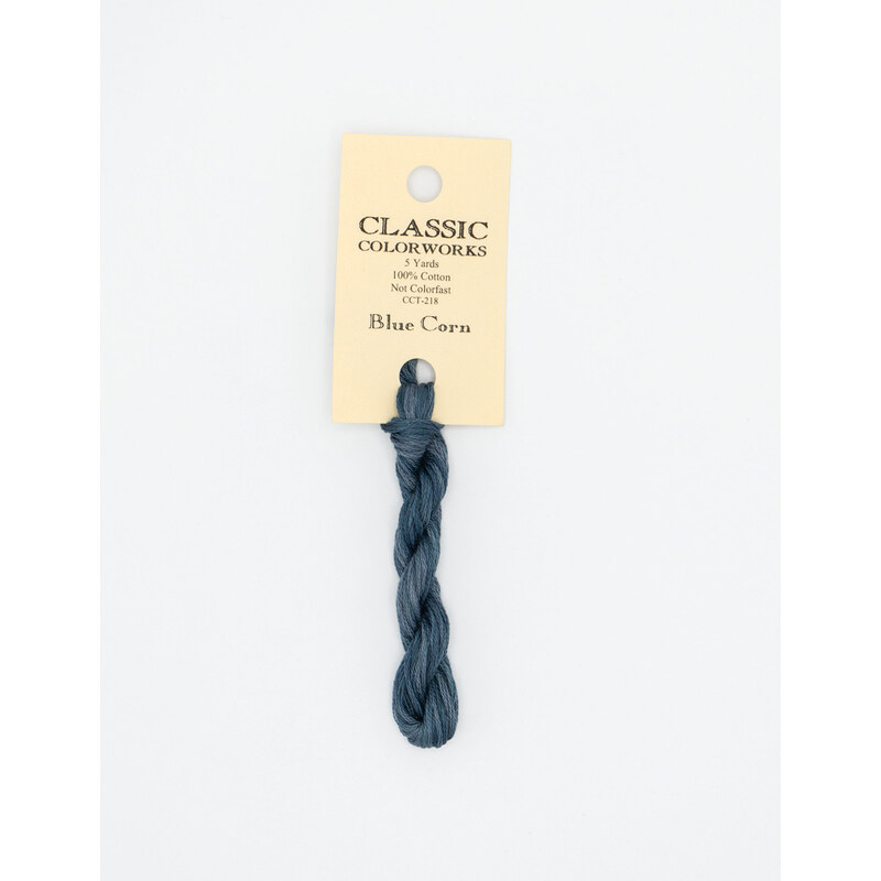A skein of indigo blue embroidery floss, twisted and bundled, with a cream and black label featuring the brand name and color information.