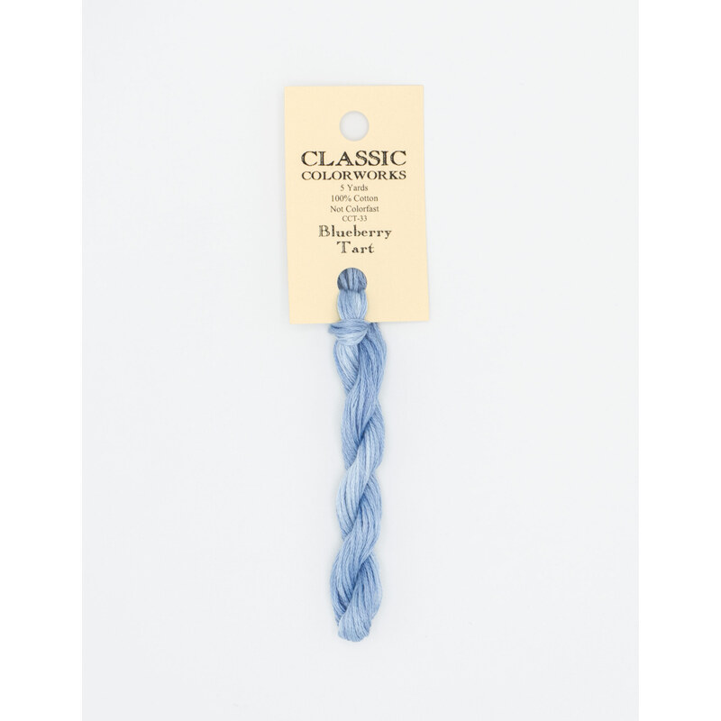A skein of blue embroidery floss, twisted and bundled, with a cream and black label featuring the brand name and color information.