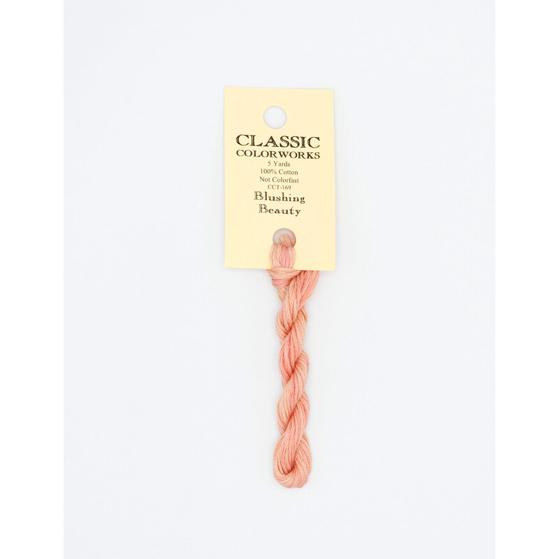 A skein of peach pink embroidery floss, twisted and bundled, with a cream and black label featuring the brand name and color information.