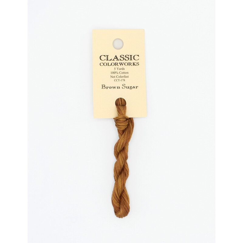 A skein of medium brown embroidery floss, twisted and bundled, with a cream and black label featuring the brand name and color information.