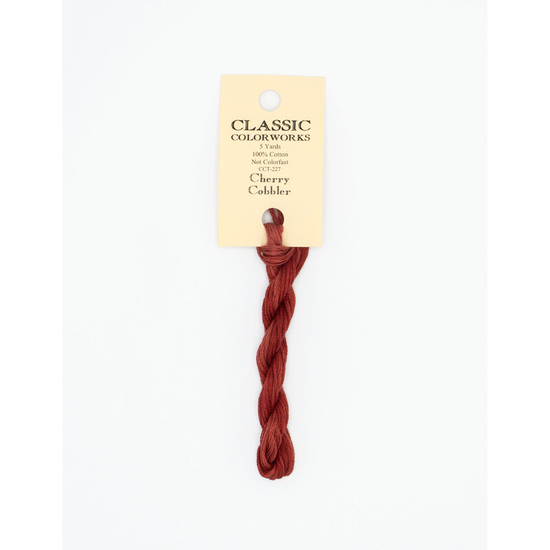 A skein of cherry red embroidery floss, twisted and bundled, with a cream and black label featuring the brand name and color information.