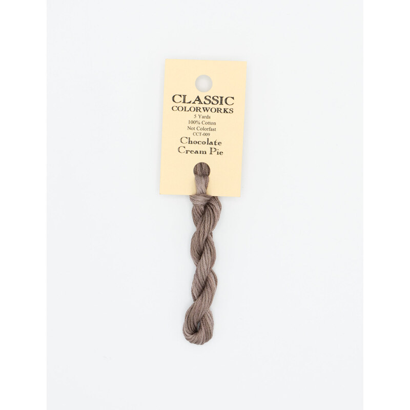 A skein of light brown gray embroidery floss, twisted and bundled, with a cream and black label featuring the brand name and color information.