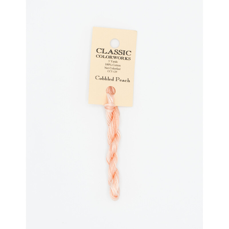 A skein of light peach embroidery floss, twisted and bundled, with a cream and black label featuring the brand name and color information.
