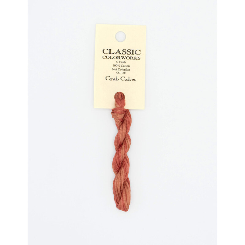 A skein of variegated muted red embroidery floss, twisted and bundled, with a cream and black label featuring the brand name and color information.