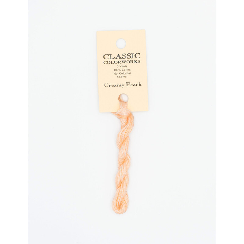 A skein of light peach embroidery floss, twisted and bundled, with a cream and black label featuring the brand name and color information.