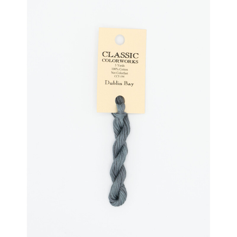 A skein of muted cobalt blue embroidery floss, twisted and bundled, with a cream and black label featuring the brand name and color information.