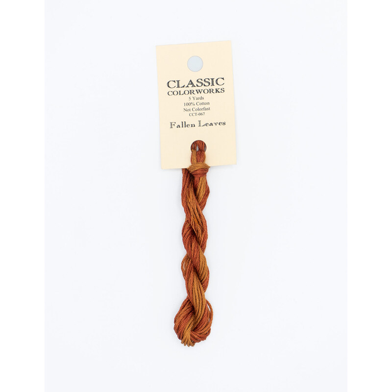 A skein of variegated orange embroidery floss, twisted and bundled, with a cream and black label featuring the brand name and color information.