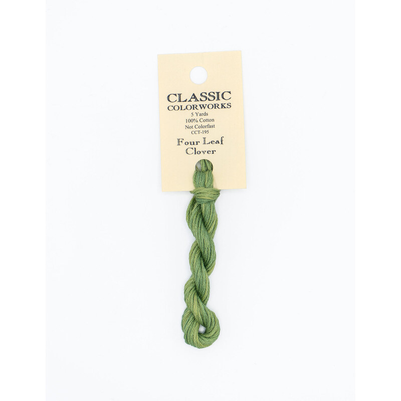 A skein of green embroidery floss, twisted and bundled, with a cream and black label featuring the brand name and color information.