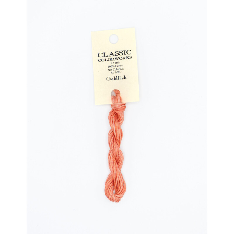 A skein of coral orange embroidery floss, twisted and bundled, with a cream and black label featuring the brand name and color information.