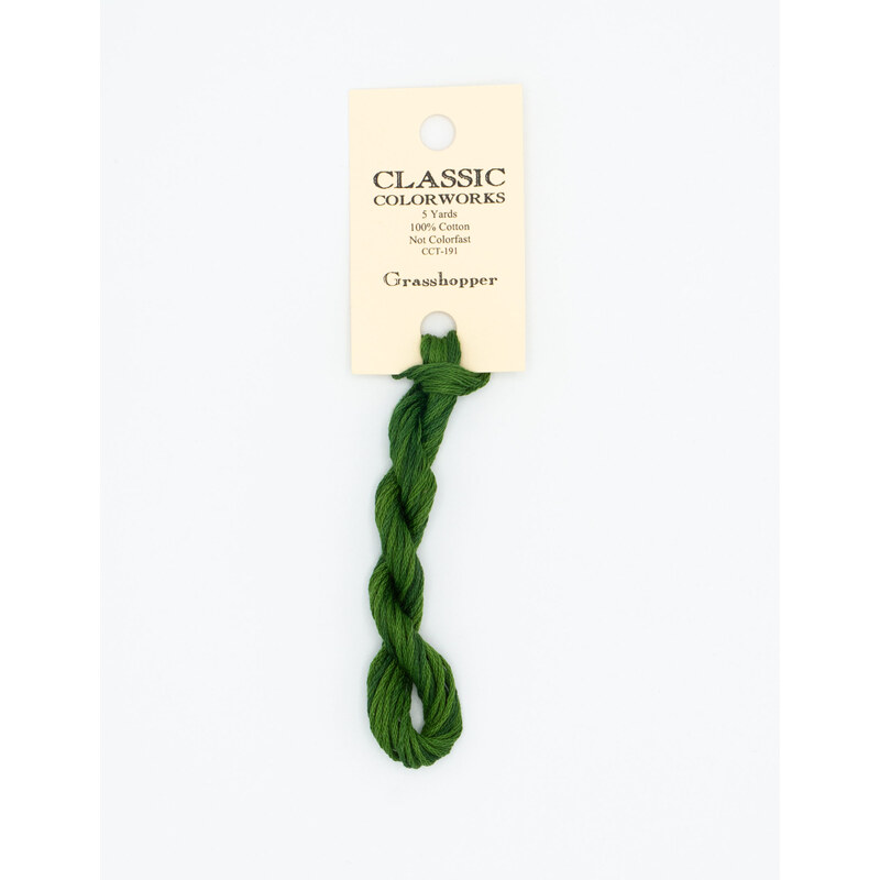 A skein of green embroidery floss, twisted and bundled, with a cream and black label featuring the brand name and color information.